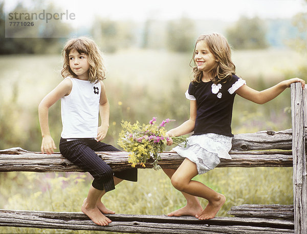 2 Mädchen sitzen auf einem Zaun