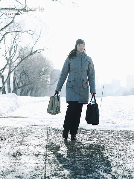 Junge Frau mit Einkaufstüten auf schneebedecktem Weg