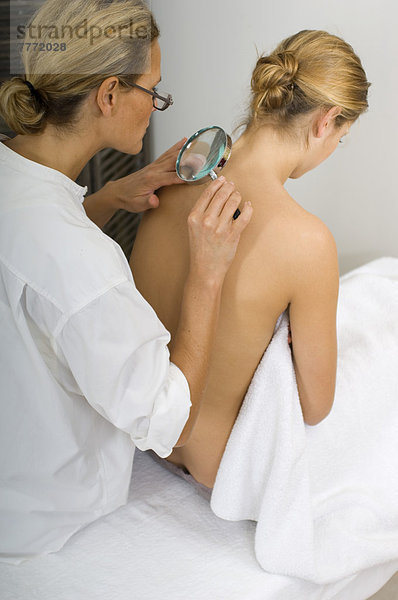 Ärztin untersucht Schönheitsflecken mit Lupe auf dem Rücken der Frau