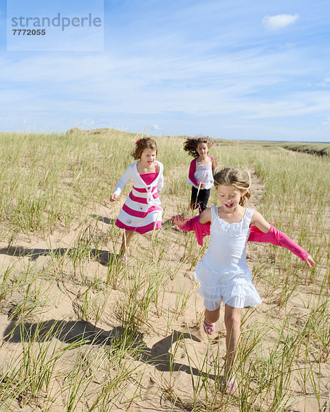 Drei kleine Mädchen  die in der Sanddüne rennen.