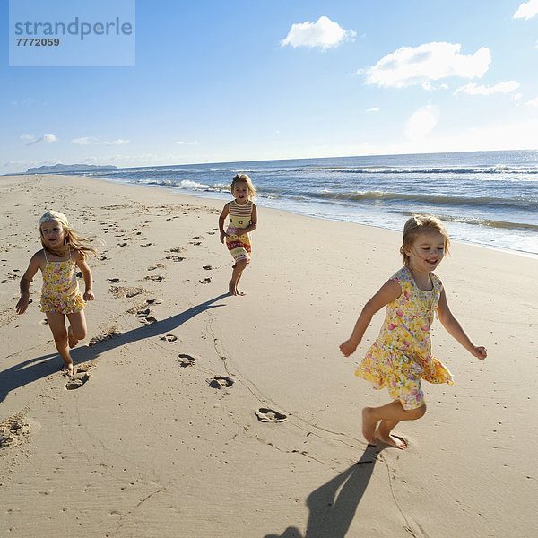 Drei kleine Mädchen  die am Strand rennen.