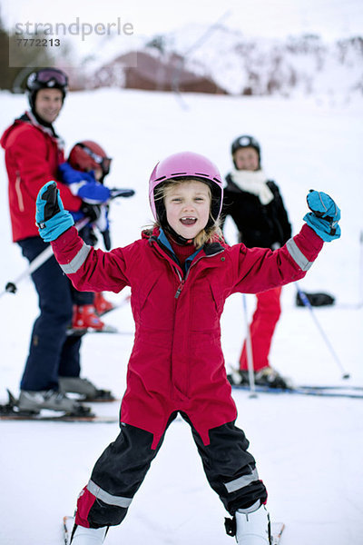 Porträt eines glücklichen Mädchens  das mit der Familie im Hintergrund Ski fährt.