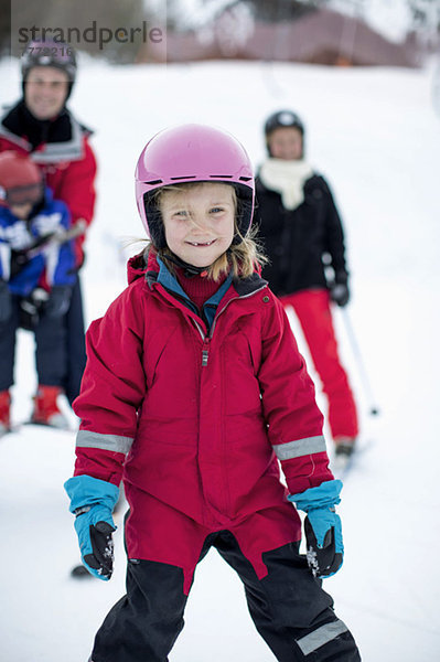 Porträt eines Mädchens in Skikleidung mit Familie im Hintergrund