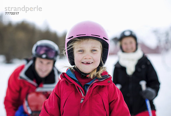 Porträt des kleinen Mädchens in Skikleidung lächelnd mit Familie im Hintergrund
