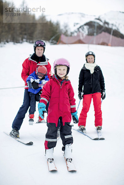 Porträt des glücklichen Mädchens in Skikleidung stehend mit Familie im Hintergrund