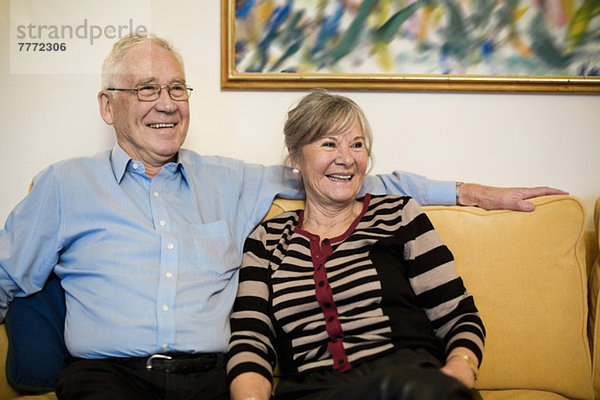 Glückliches Senior-Paar schaut weg  während es auf dem Sofa sitzt.