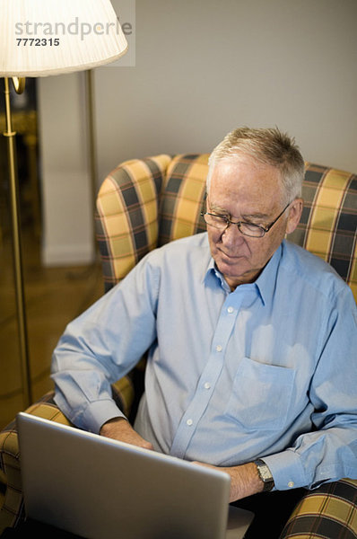 Senior Mann mit Laptop auf Sessel