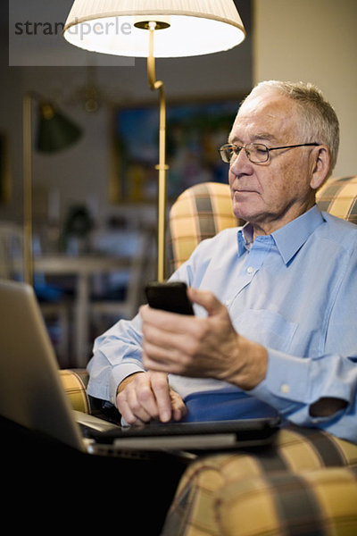 Senior-Mann mit Laptop  Handy und digitalem Tablett im Sessel