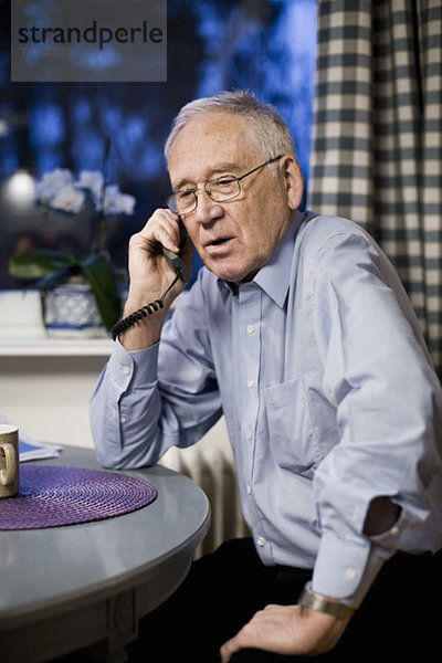 Älterer Mann mit Telefon am Tisch