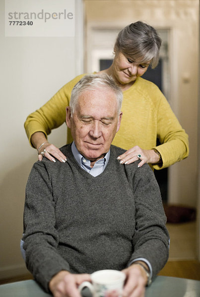 Seniorin gibt dem Mann zu Hause eine Schultermassage