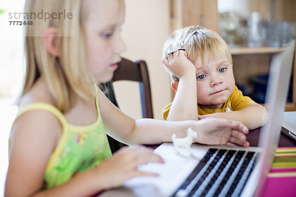 Kleiner Junge sitzend mit Schwester am Tisch mit Laptop