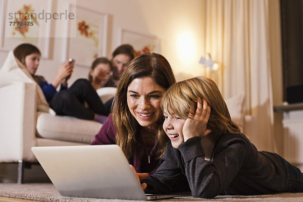 Glückliche Mutter und Sohn mit Laptop auf dem Boden mit Familie auf dem Sofa im Hintergrund