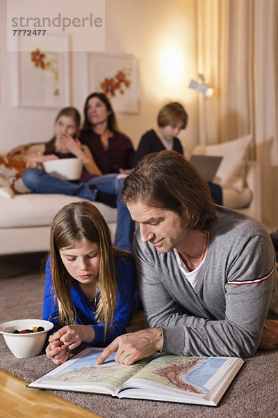 Vater und Tochter lesen Karte auf dem Boden mit Familie auf dem Sofa im Hintergrund