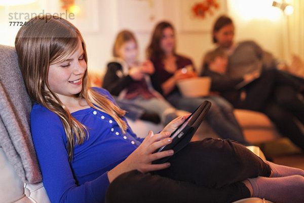 Fröhliches Mädchen mit digitalem Tablett und Familie auf dem Sofa im Wohnzimmer