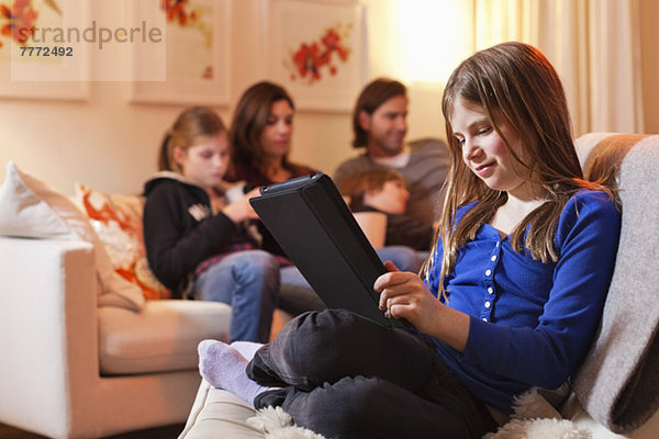 Mädchen mit digitalem Tablett und Familie auf dem Sofa im Wohnzimmer