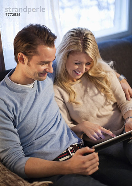 Glückliches Paar mit digitalem Tablett auf dem Sofa im Wohnzimmer