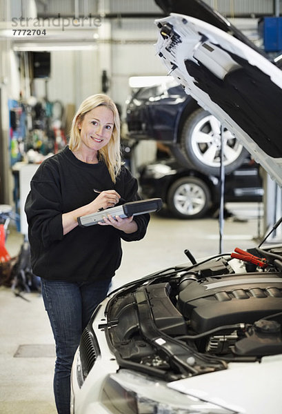 Porträt einer mittleren erwachsenen Mechanikerin  die ein digitales Tablett hält  während sie bei geöffneter Motorhaube steht.