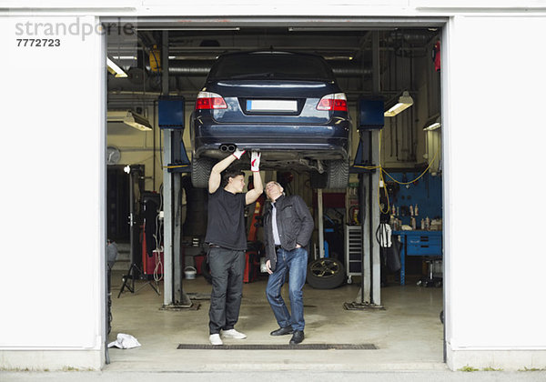 Junger Mechaniker erklärt dem Kunden in der Autowerkstatt Probleme mit dem Auto