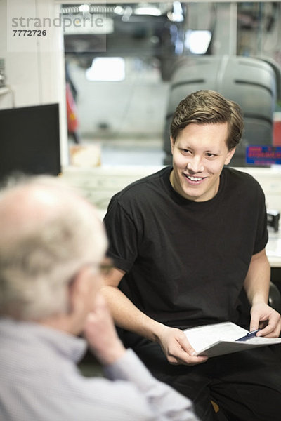 Fröhlicher junger Mechaniker im Gespräch mit dem Kunden im Büro