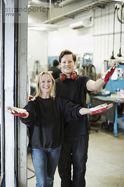 Porträt von glücklichen Mechanikern  die mit erhobenen Armen in der Werkstatt stehen.