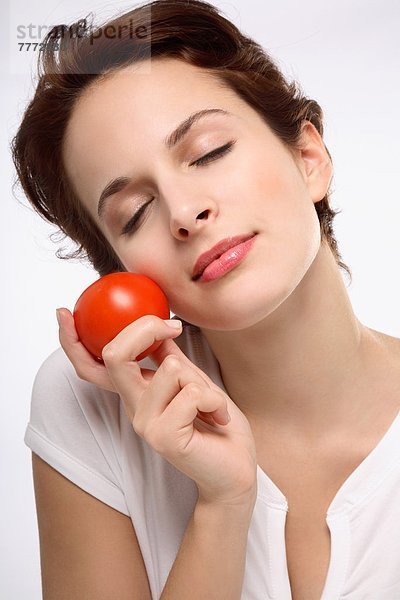 Porträt einer jungen brünetten Frau  Augen geschlossen  Tomate gegen Gesicht haltend