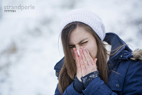 Junge Frau in Winterkleidung schnäuzt sich die Nase