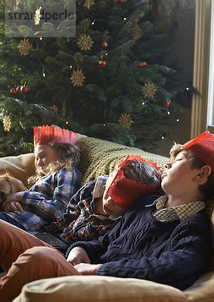 Kinder in Papierkronen schlafen auf dem Sofa