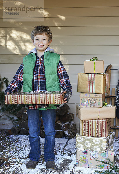 Junge mit Weihnachtsgeschenken auf verschneiter Veranda