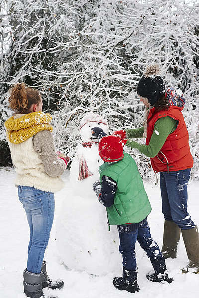 Mutter und Kinder machen Schneemann im Freien