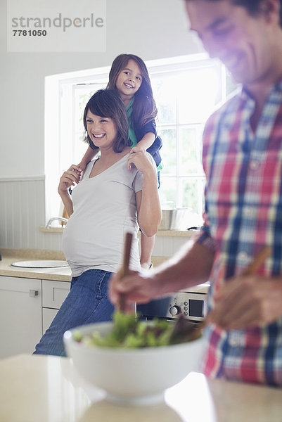 Schwangere Mutter und Tochter sehen Vater beim Salatwerfen zu.