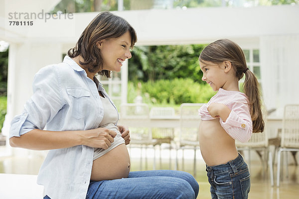 Mädchen und schwangere Mutter vergleichen Bäuche