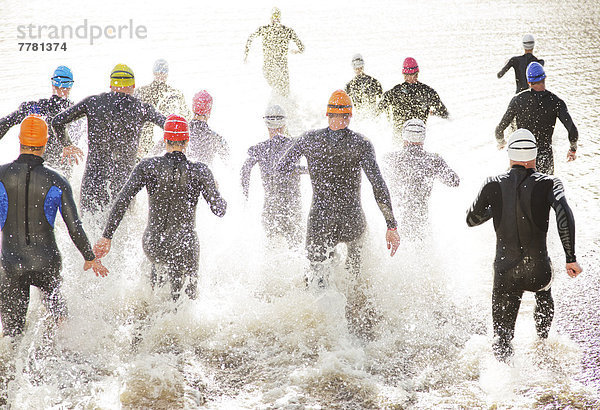 Triathleten in Trikots  die in den Ozean laufen.