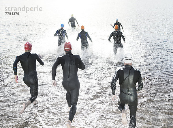 Triathleten in Trikots  die in den Ozean laufen.