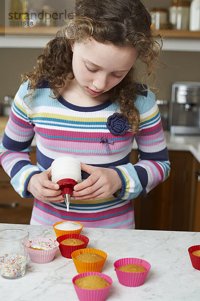 Mädchen dekorieren Muffins in der Küche