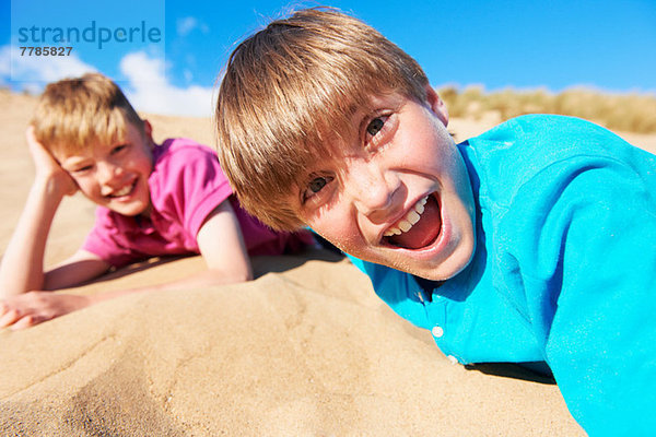 Zwei blondhaarige Jungen liegen am Strand.