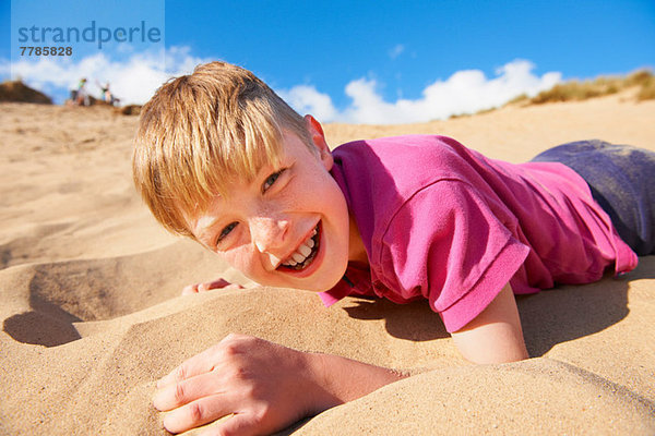 Blondhaariger Junge am Strand liegend