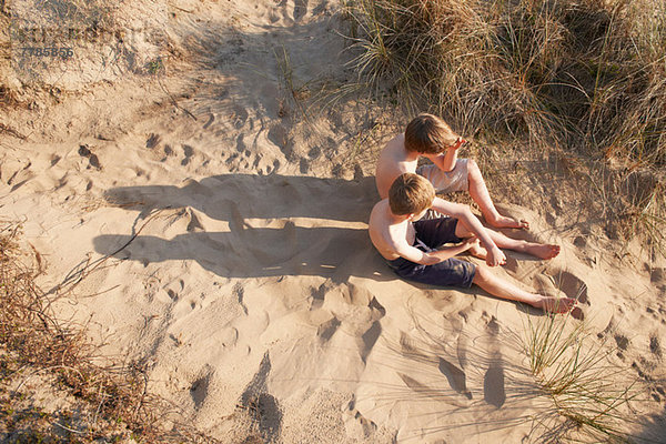 Zwei Jungen sitzen am Strand  hoher Winkel