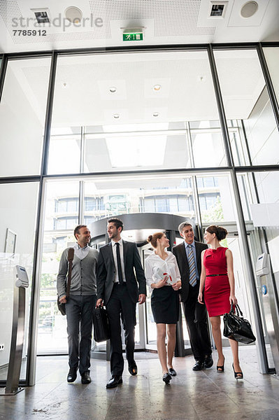 Gruppe von Geschäftsleuten  die sich unterhalten und in ein gläsernes Bürogebäude eintreten.