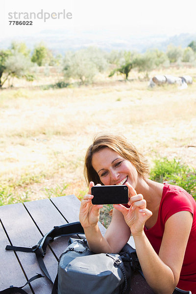 Frau sitzt an der Picknickbank und fotografiert sich selbst mit Fotohandy.