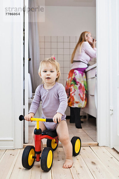 Kleinkind Mädchen spielt auf Dreirad  Mutter im Hintergrund