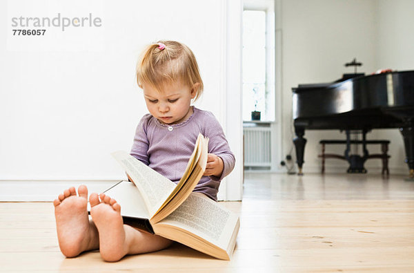 Kleinkind Mädchen sitzend auf dem Boden Lesebuch