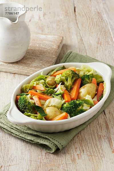 Gemüseauswahl bestehend aus Brokkoli  Karotten  neuen Kartoffeln und Kohl in weißer Servierplatte auf grünem Tuch