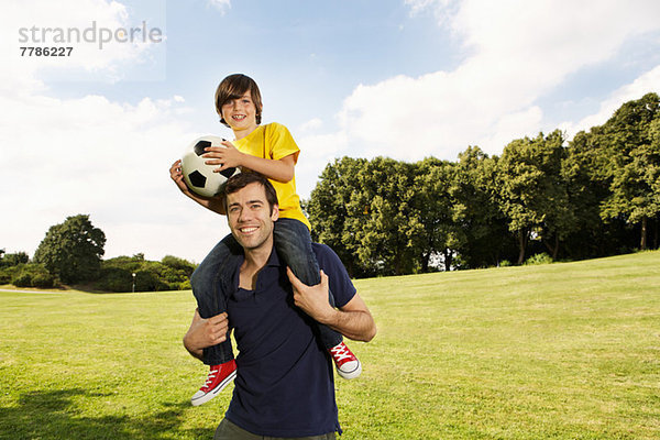 Vater trägt Sohn auf Schultern mit Fußball