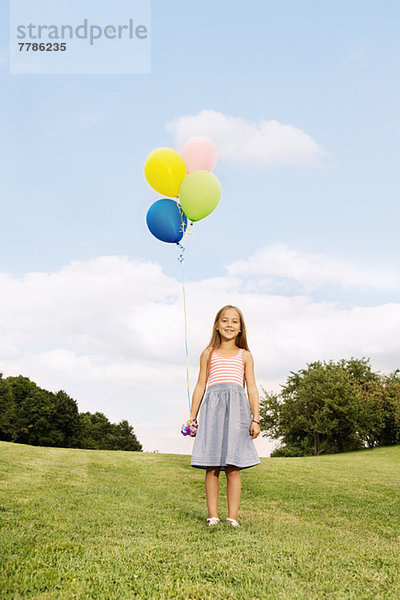 Mädchen hält Luftballons auf Gras stehend