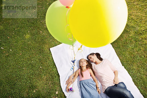 Mutter und Tochter liegen auf einer Decke und halten Luftballons  hoher Winkel