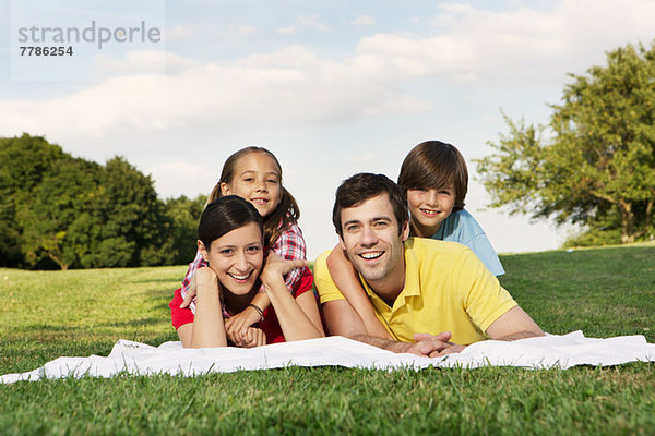 Porträt einer Familie mit zwei Kindern auf Gras liegend