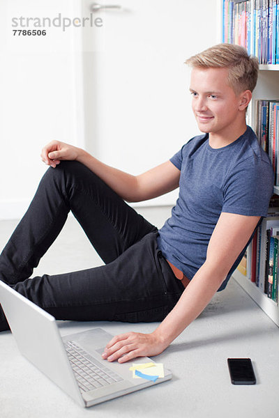 Junger Mann auf dem Boden sitzend mit Laptop