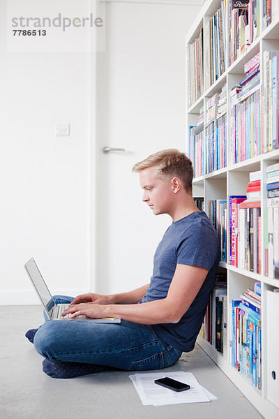Junger Mann auf dem Boden sitzend mit Laptop