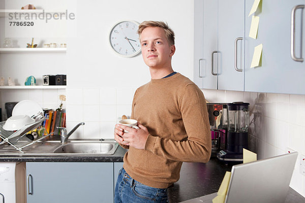 Junger Mann in der Küche mit Kaffeetasse