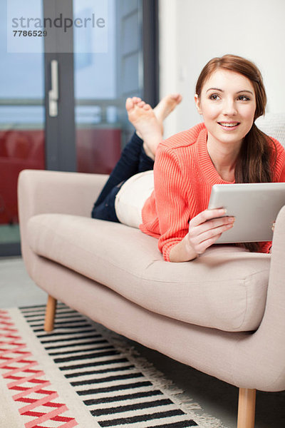 Junge Frau auf dem Sofa liegend mit digitalem Tablett